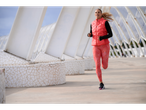 Mulher com colete de treino Crivit coral e leggings estampadas a correr ao ar livre.