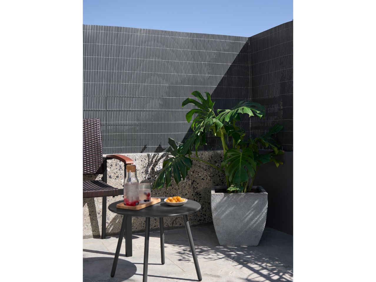Outdoor patio with a plant in a pot, a small table with drinks and snacks, and a chair.