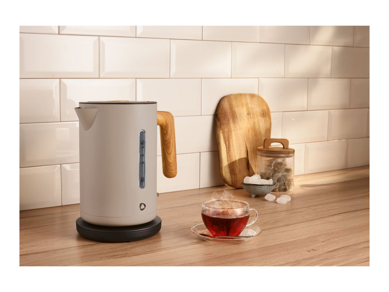 Kettle with wooden handle, steaming tea cup, and sugar on a kitchen counter.