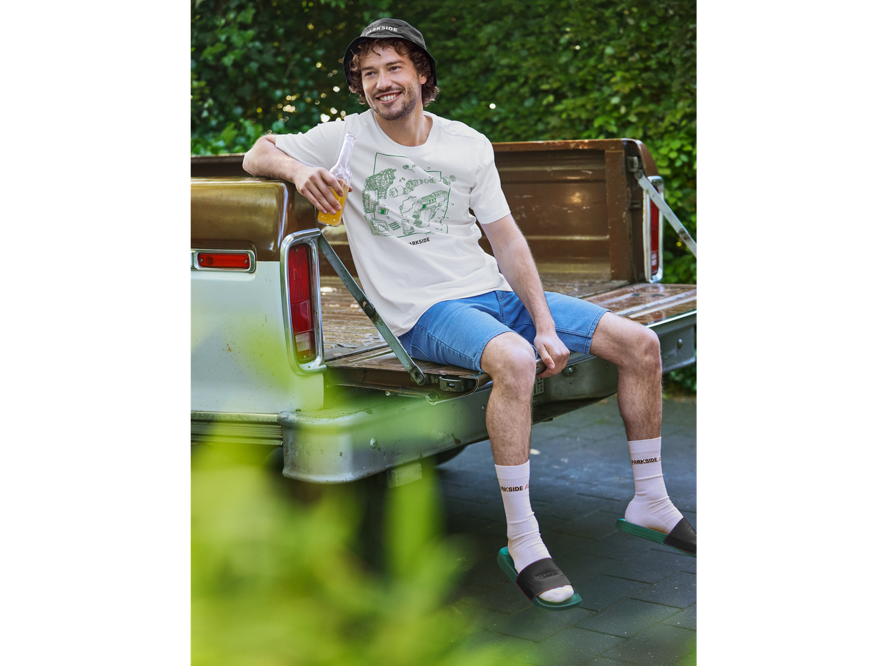 Homem com camiseta branca Parkside sentado na caçamba de uma caminhonete antiga.