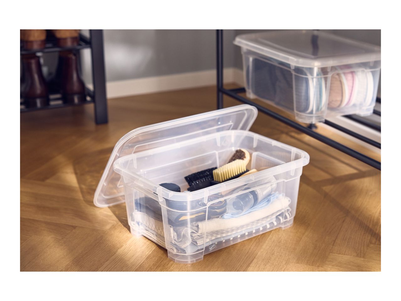 Clear plastic storage boxes with lids, filled with shoes and shoe care accessories.
