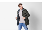 A man in a dark green jacket, light grey sweater, and blue jeans.