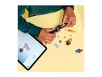 Child building a toy motorcycle with a tablet showing instructions, surrounded by toy figures.