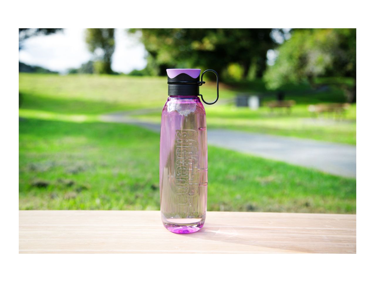 A purple reusable water bottle filled with water on a wooden table in a park.