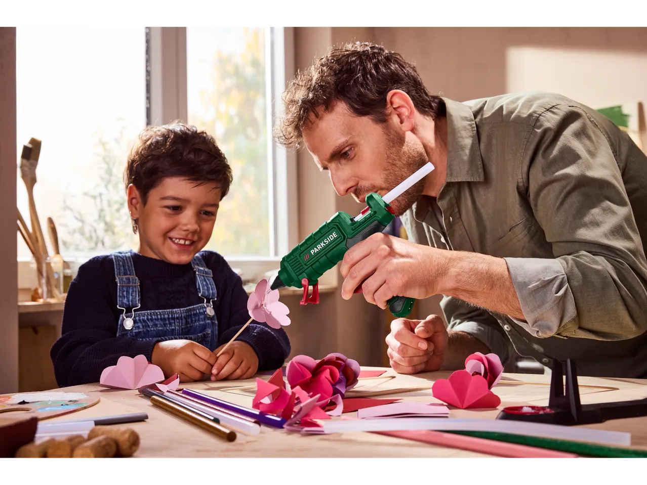 Apa és gyermeke forró ragasztópisztollyal készítenek papírdíszeket.