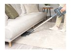 A person vacuuming under a sofa with a cordless stick vacuum cleaner.