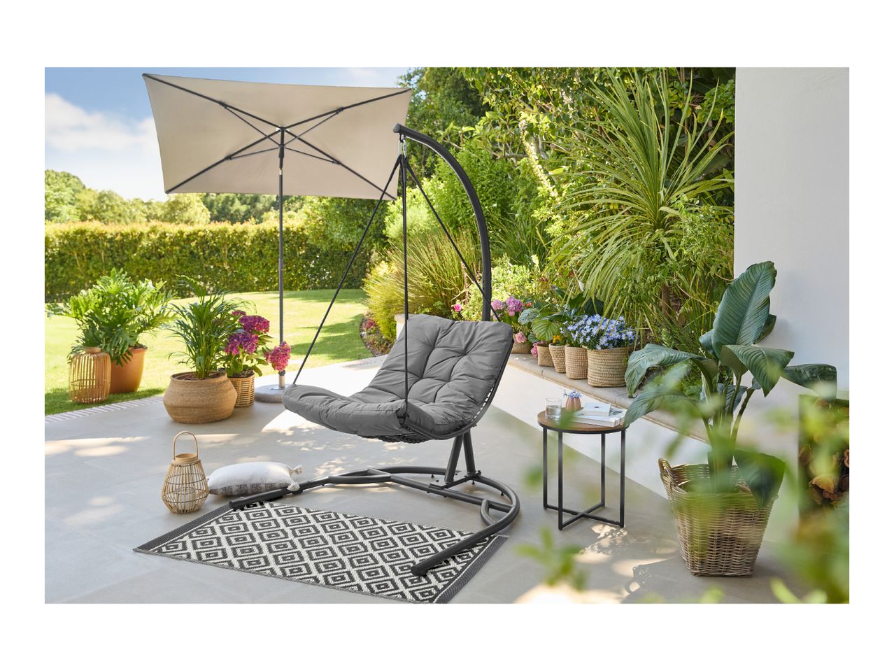 Outdoor patio with a hanging egg chair, umbrella, side table, and potted plants.