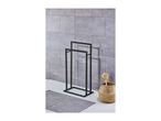 Black metal towel rack next to a woven basket with a body brush and a gray bath mat.