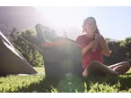 Woman in a Crivit sports top, sitting by a tent and cooler, holding a drink.