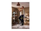 Man on a stepladder changing a lightbulb in a workshop with shelving and tools.