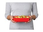 Person holding a red rectangular food container filled with pasta, cherry tomatoes, and herbs.