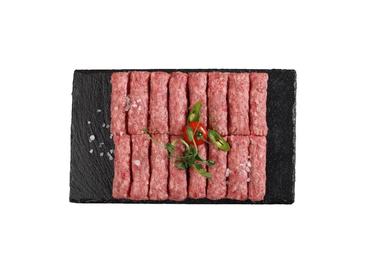 Sveži ćevapi na crnoj ploči sa solju, čilijem i paradajzom.