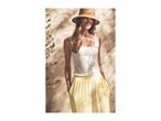 Woman in straw hat, white tank top, and yellow wide-leg pants, standing in dappled sunlight.