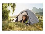 Woman relaxing in a grey camping tent in a grassy field with mountains in the background.