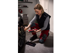 Woman inflating car tire with a portable air compressor in a garage.