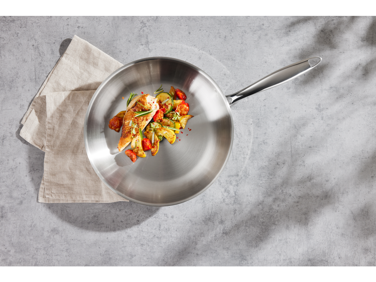 Tigaie din oțel inoxidabil cu pește și legume prăjite pe o masă de beton.