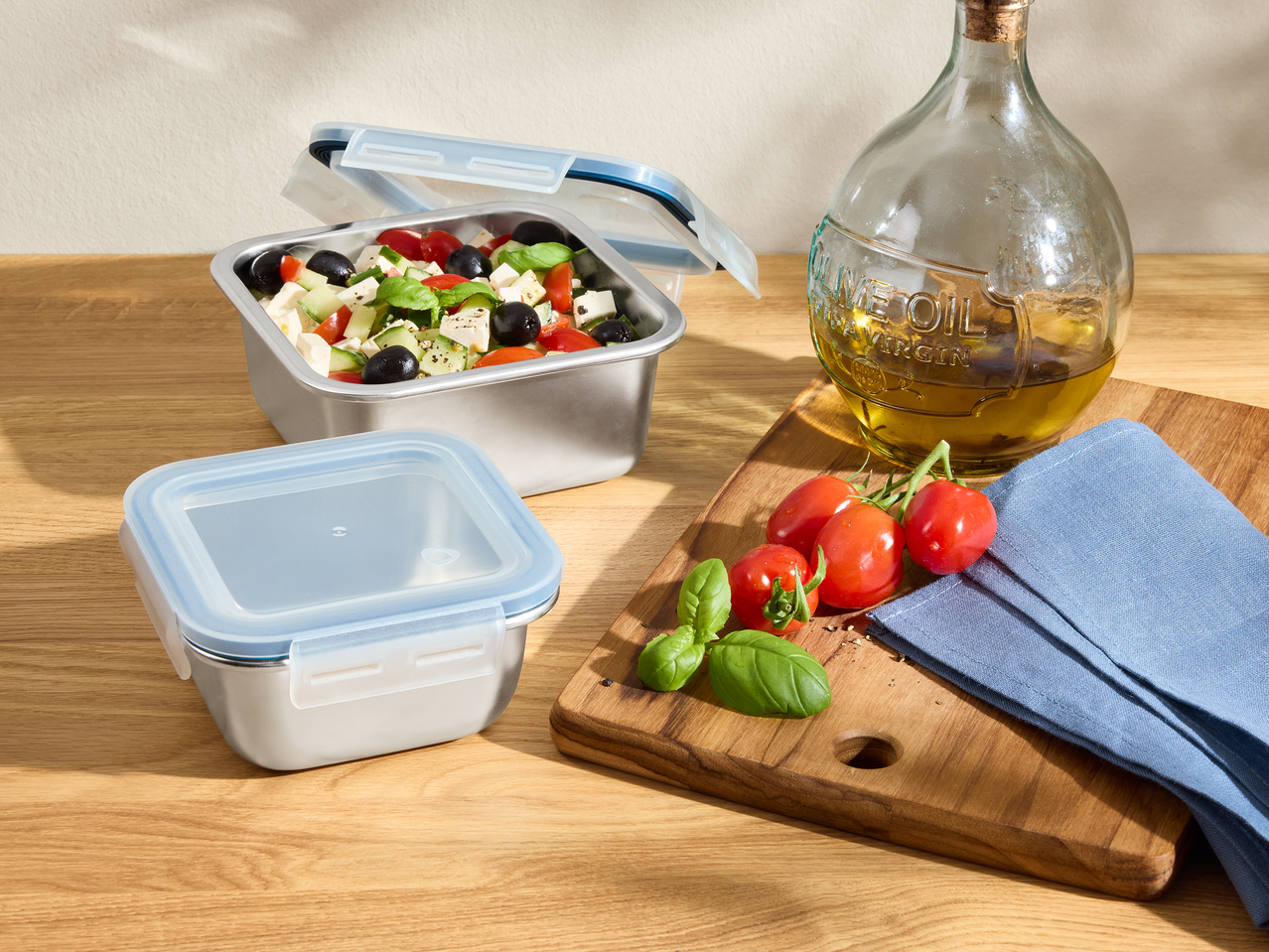 Ανοξείδωτα δοχεία φαγητού με φρέσκια σαλάτα, ελαιόλαδο, ντομάτες και βασιλικό σε ξύλινο τραπέζι.