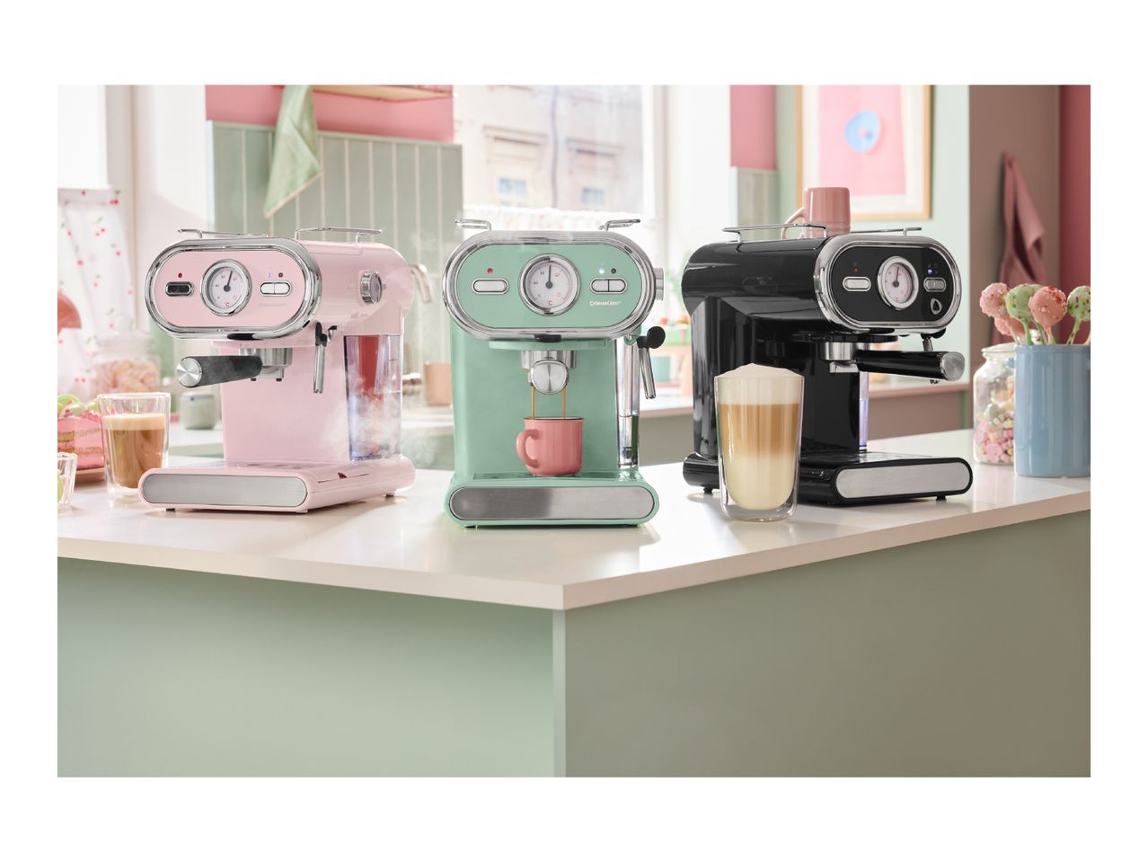 Three SilverCrest espresso machines in pink, mint green, and black on a kitchen counter.