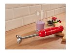 Red hand blender on a wooden countertop next to a beaker with a purple smoothie