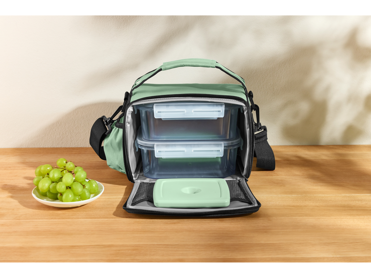 Silvercrest® torba za ručak sa dve posude za hranu i tanjirom zelenog grožđa na drvenom stolu.