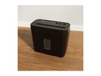 Black paper shredder with a clear window on a wooden floor next to a white wall.