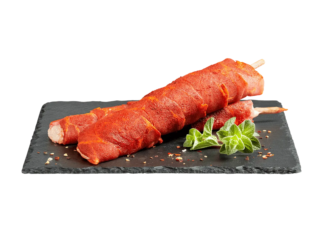 Brochettes de viande crue enrobées de bacon et saupoudrées de paprika, sur une planche en ardoise.