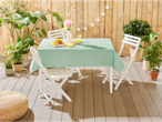 Garden table with light green tablecloth, white folding chairs, and green plants.