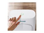 A hand presses the power button on a white Silentnight air purifier on a wooden surface.