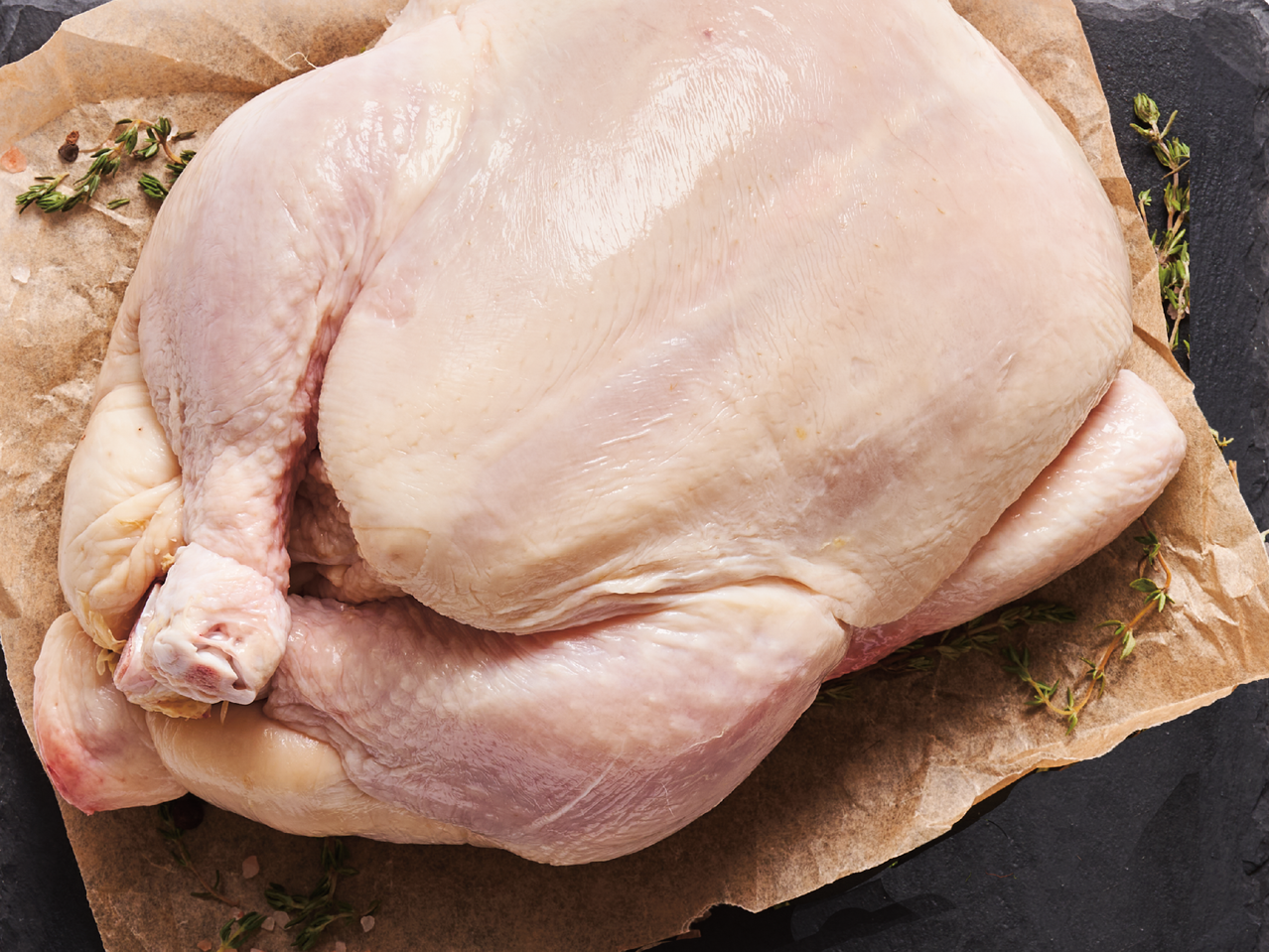 Цяло сурово пиле върху хартия за печене с мащерка и подправки.