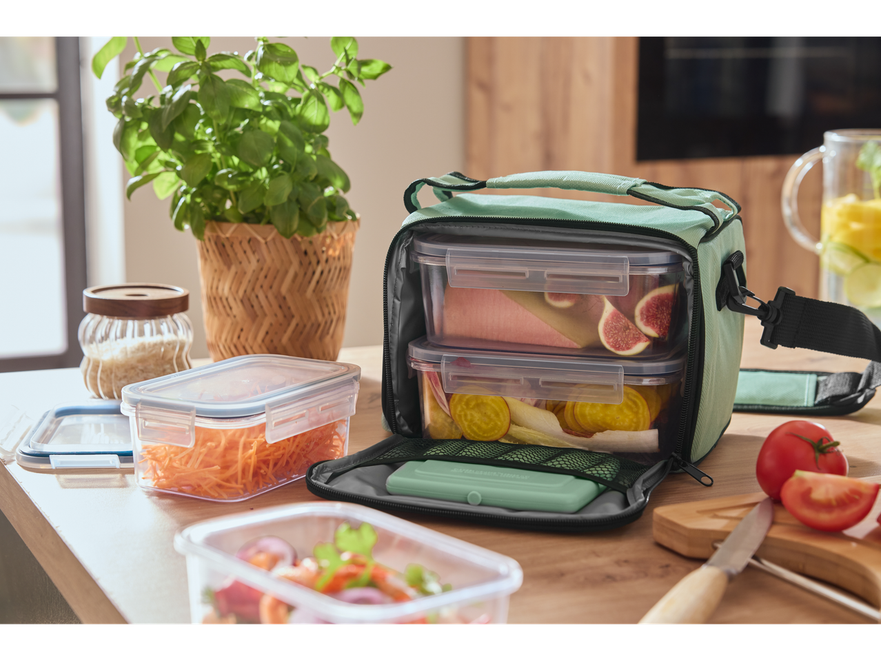 Silvercrest® torba za ručak sa posudama za hranu, svežim povrćem i bosiljkom na drvenom stolu.