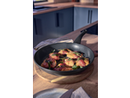 Pancetta-wrapped chicken with sage in a frying pan on a wooden board in a kitchen.