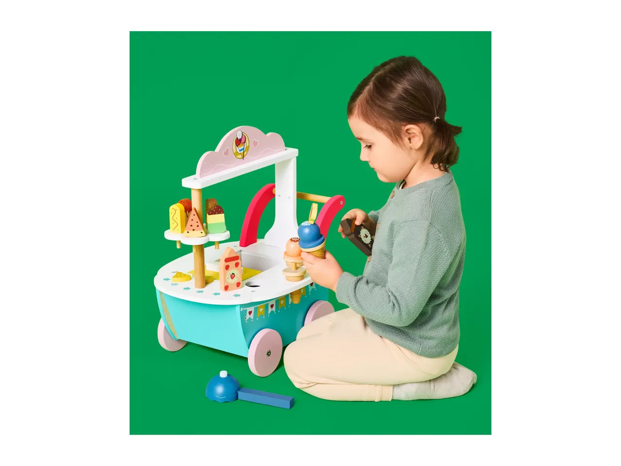Child playing with a wooden ice cream and dessert stand on a green background.