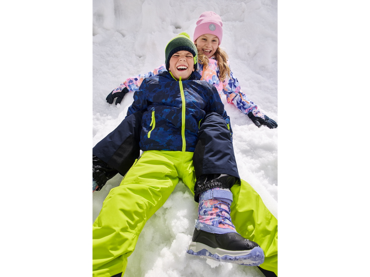 Two happy kids in CRIVIT winter boots and snow gear playing in the snow.