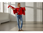 Woman in red esmara® chunky knit cardigan, red top, and jeans, holding cardigan open.