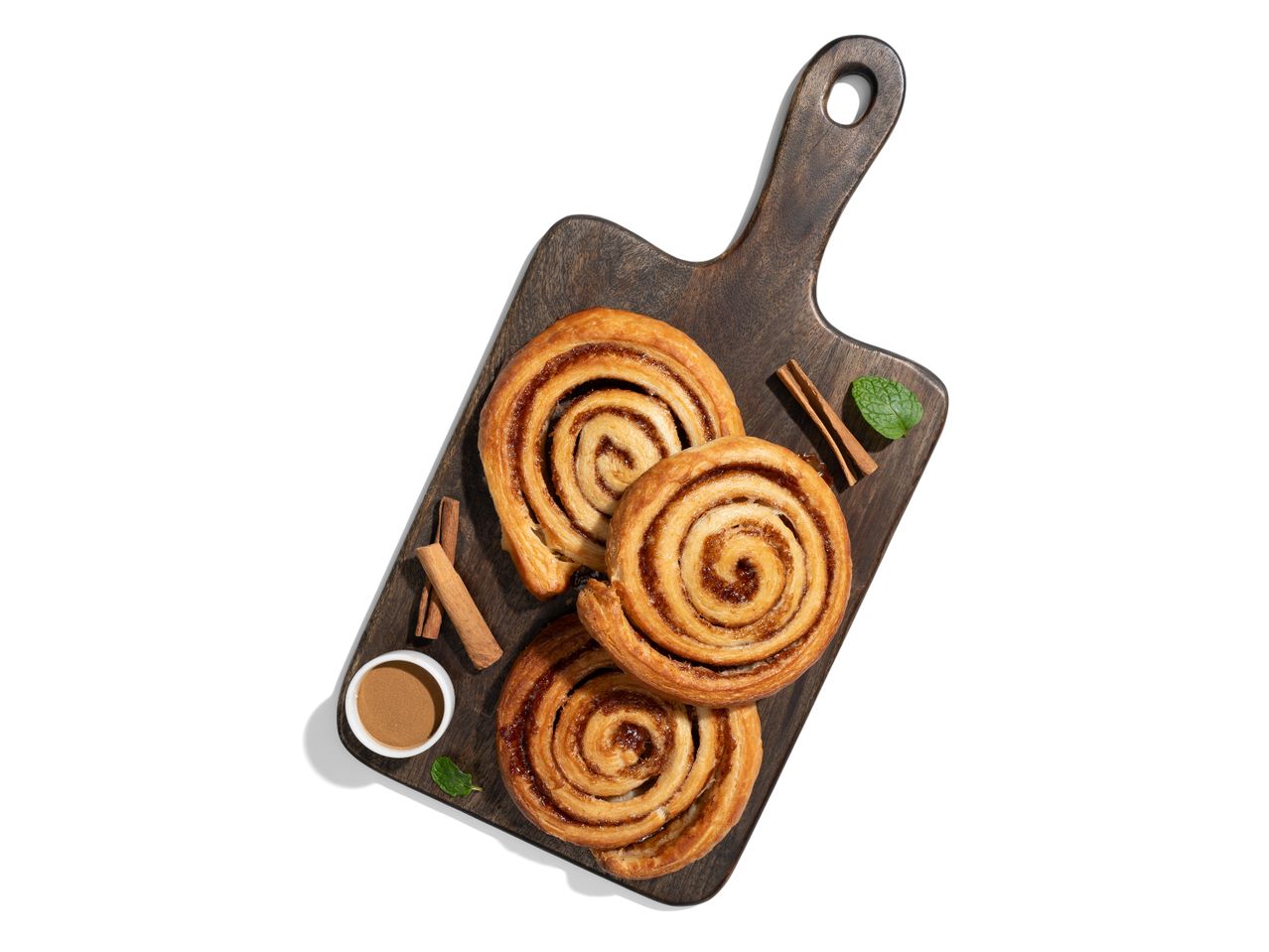 Három fahéjas csiga fából készült vágódeszkán.