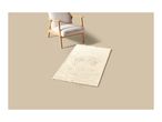 A cream-colored bath mat with a textured rose pattern next to a wooden armchair.