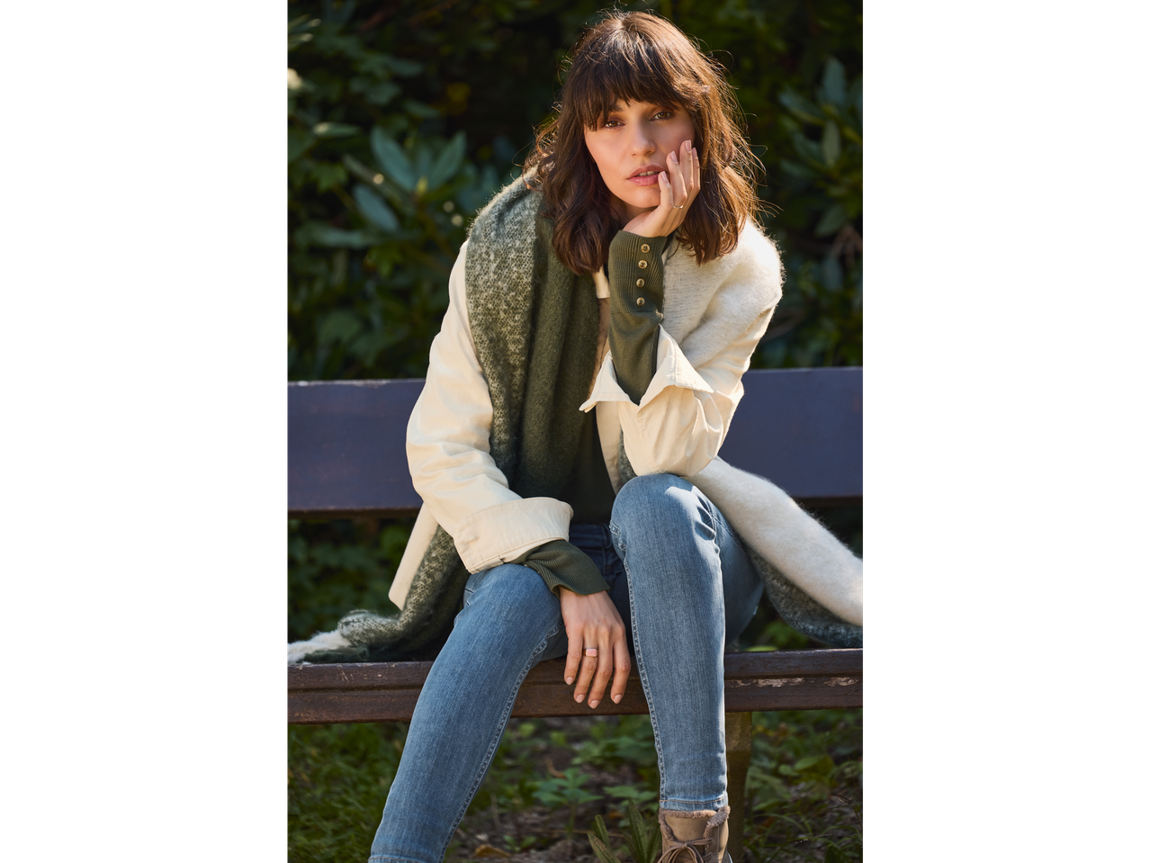 Woman in esmara® corduroy overshirt, green top, jeans, and scarf on a bench.