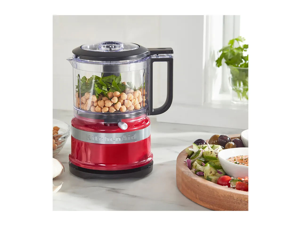 Red food processor with chickpeas and parsley, next to a salad platter.