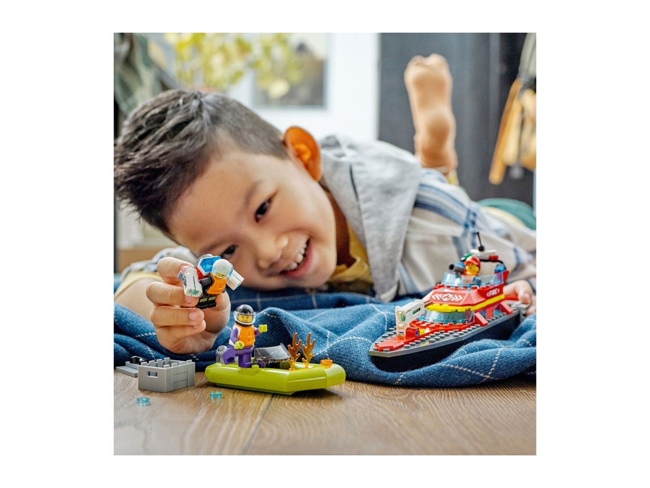 A child playing with toy boats and figures on a wooden floor.