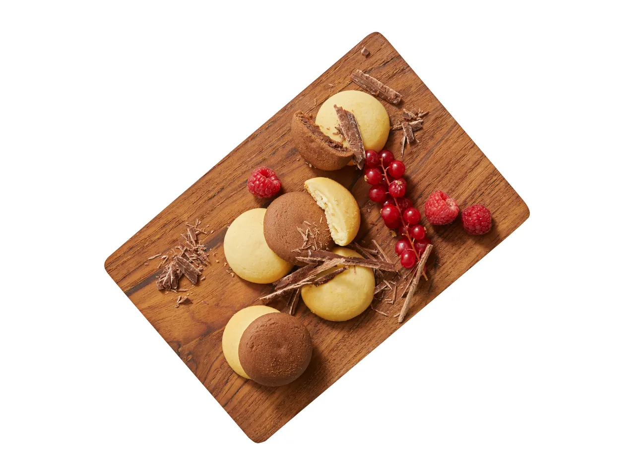 Chocolate and vanilla cookies with raspberries, redcurrants, and chocolate shavings on a wooden board.