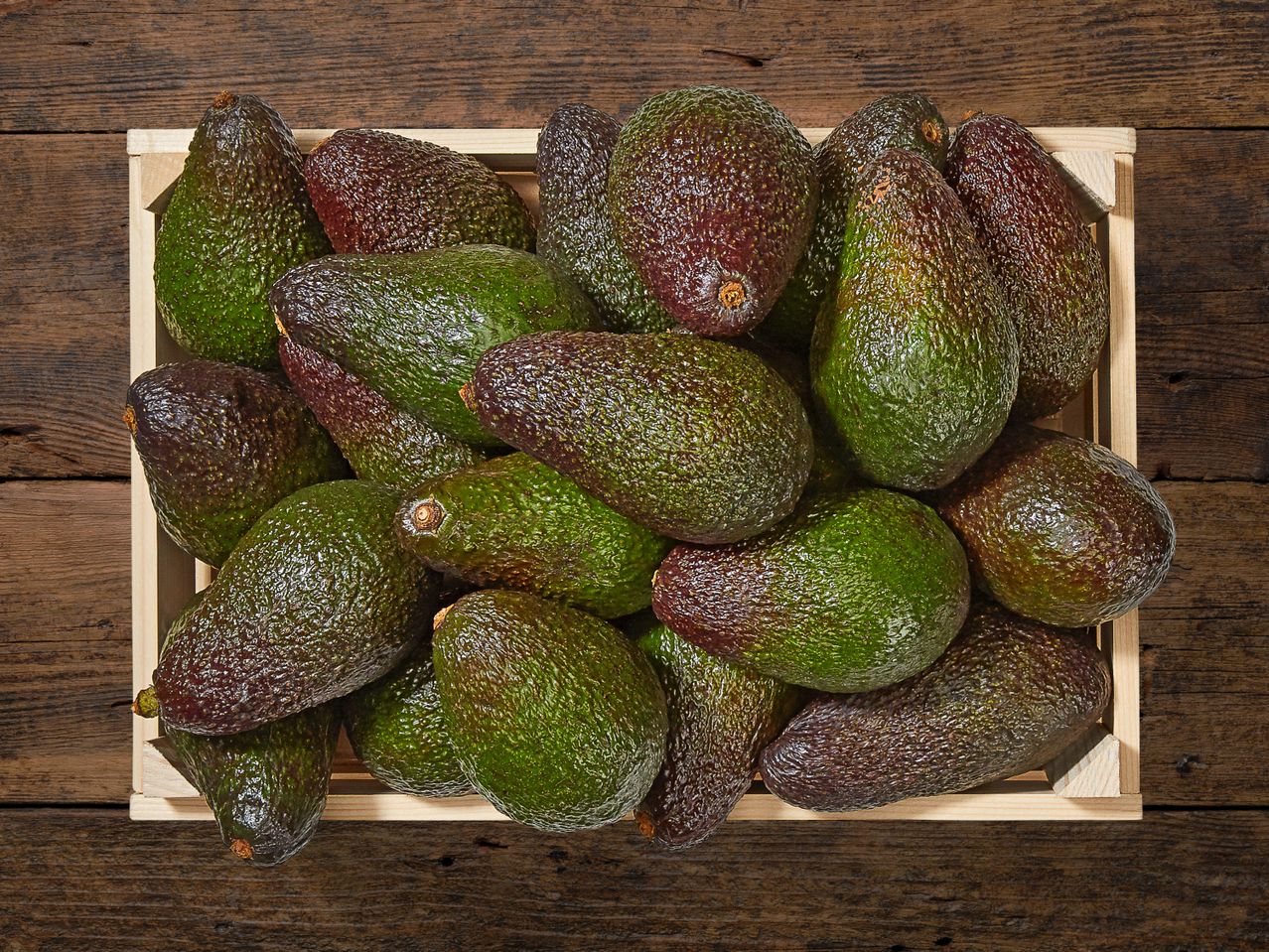 Eine Holzkiste voller reifer Avocados.