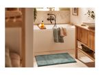 Bathroom with a white bathtub, wooden vanity, and a teal bath mat.