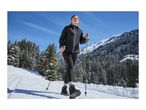 A woman winter hiking on a snowy trail with trekking poles, wearing a black jacket and leggings.