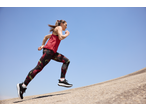 Woman in red tank top and patterned leggings running uphill against a clear blue sky.