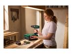 Woman holding a cordless drill, with a battery charger and drill bits on a wooden workbench.