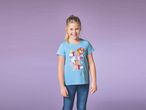 Una bambina sorridente indossa una maglietta azzurra con stampa Paw Patrol e jeans.