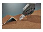 Gloved hand cutting brown carpet with a utility knife.