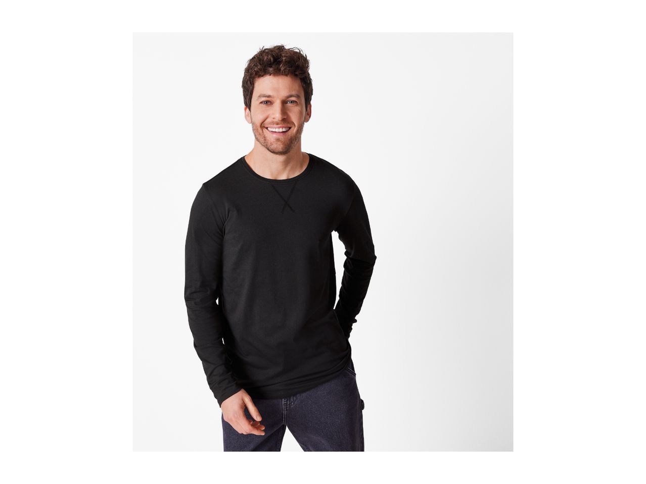 A smiling man in a black long-sleeve shirt and dark jeans.