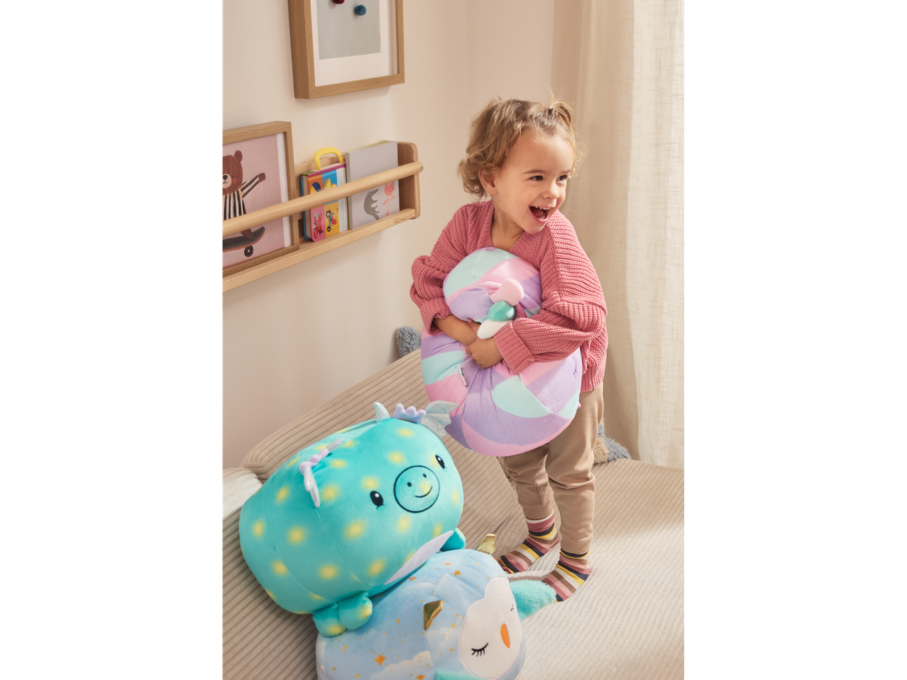 A happy child holding a Lupilu Squishy Plush Toy, with other plush toys nearby.