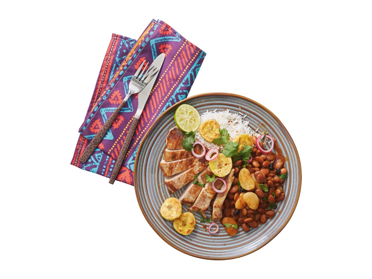 Pork loin with rice, beans, plantains, and red onion on a plate with patterned napkins and cutlery.